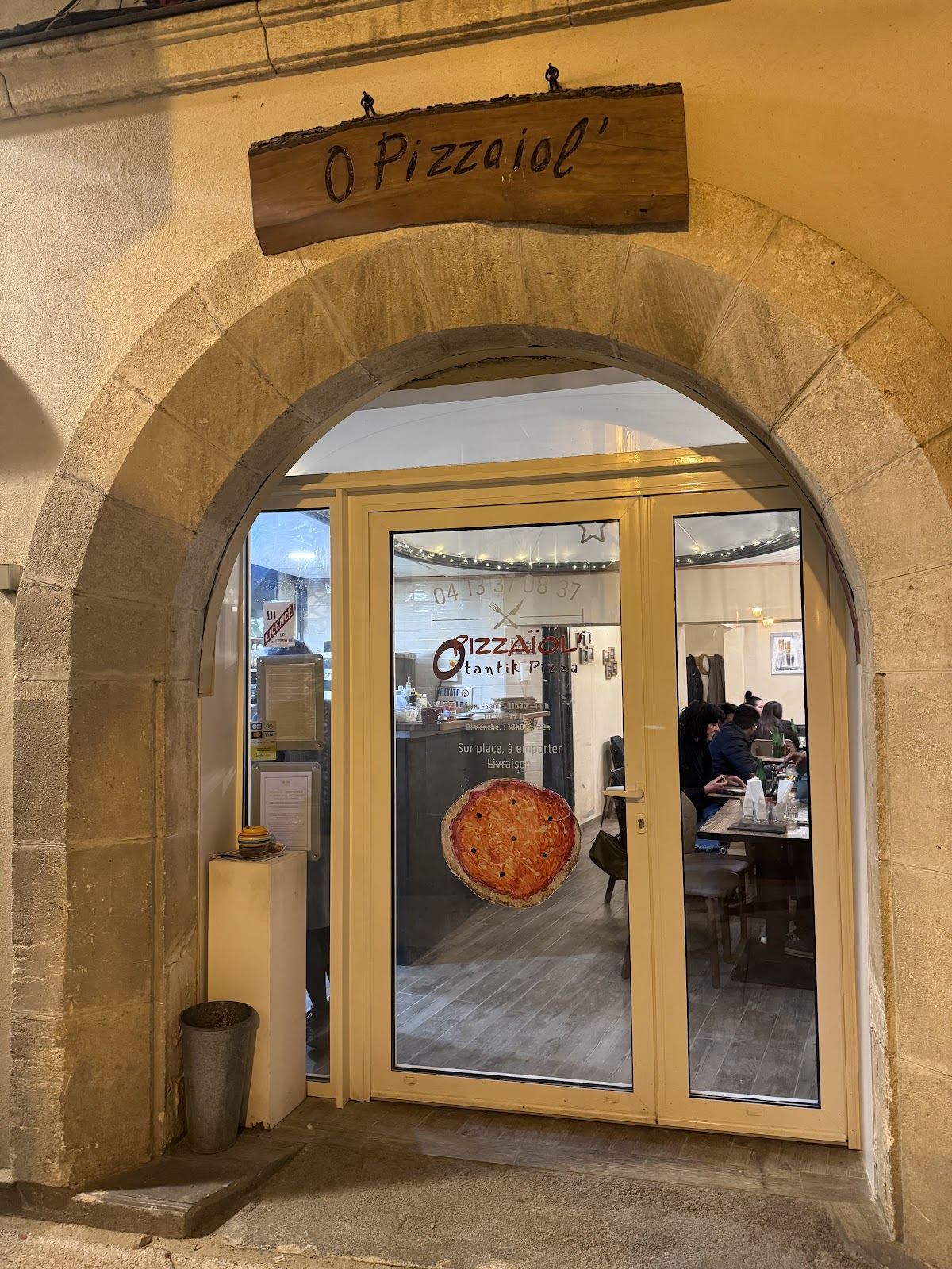 Façade en pierre de la pizzeria avec son enseigne en bois, de nuit