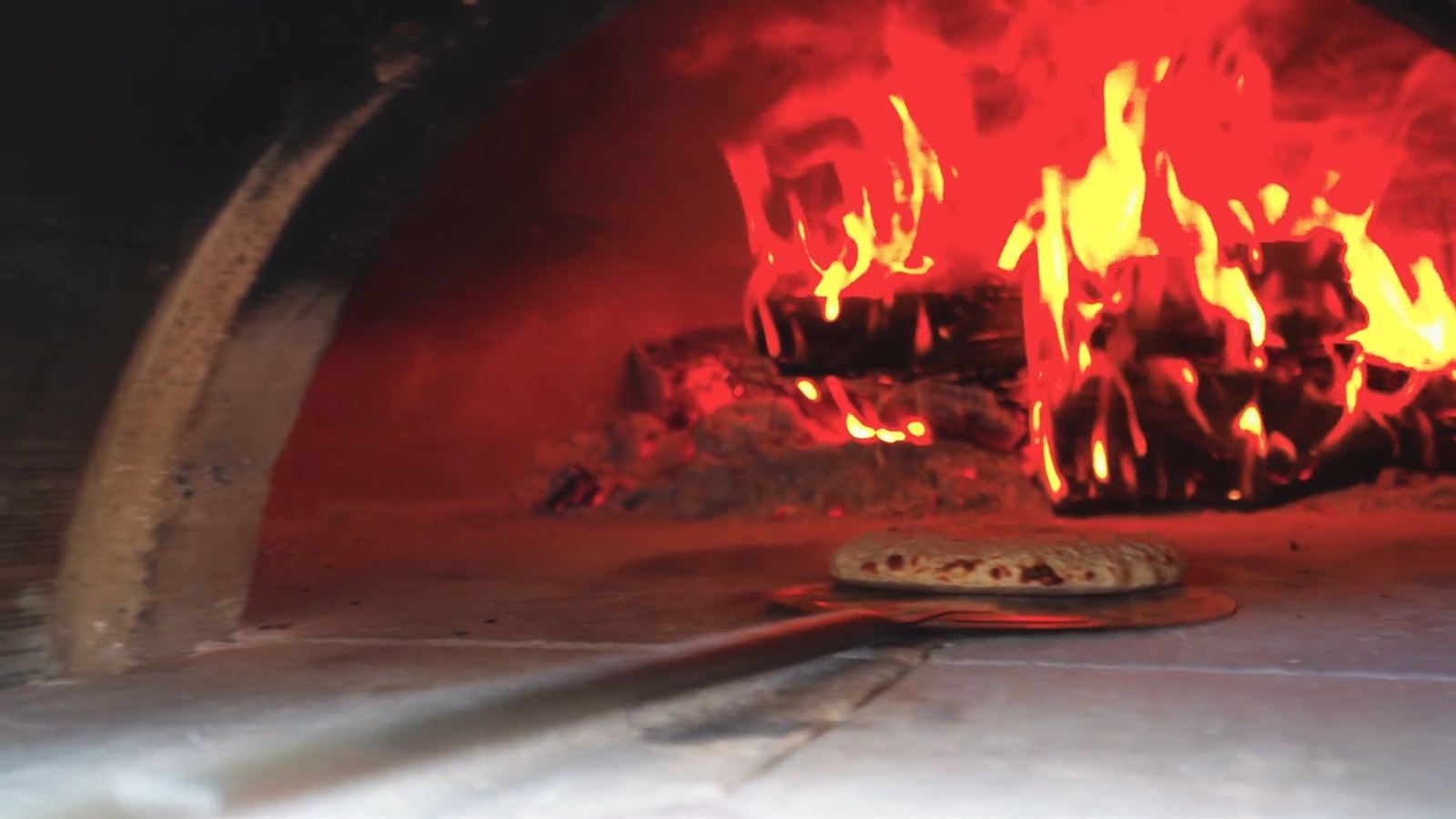 Pizza enfournée sur une pelle devant les flammes d'un four à bois