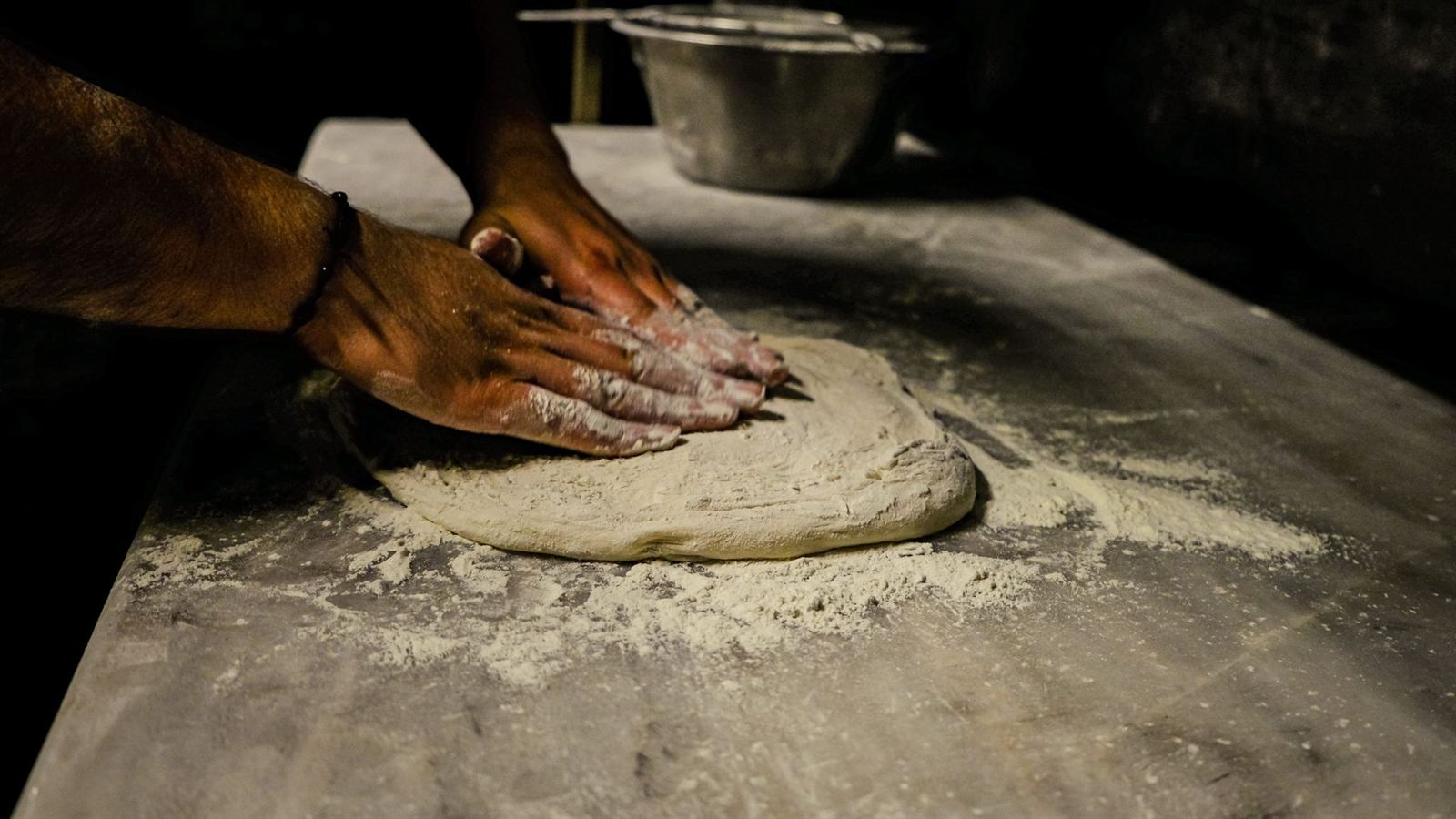 Mains pétrissant une pâte à pizza sur un plan fariné