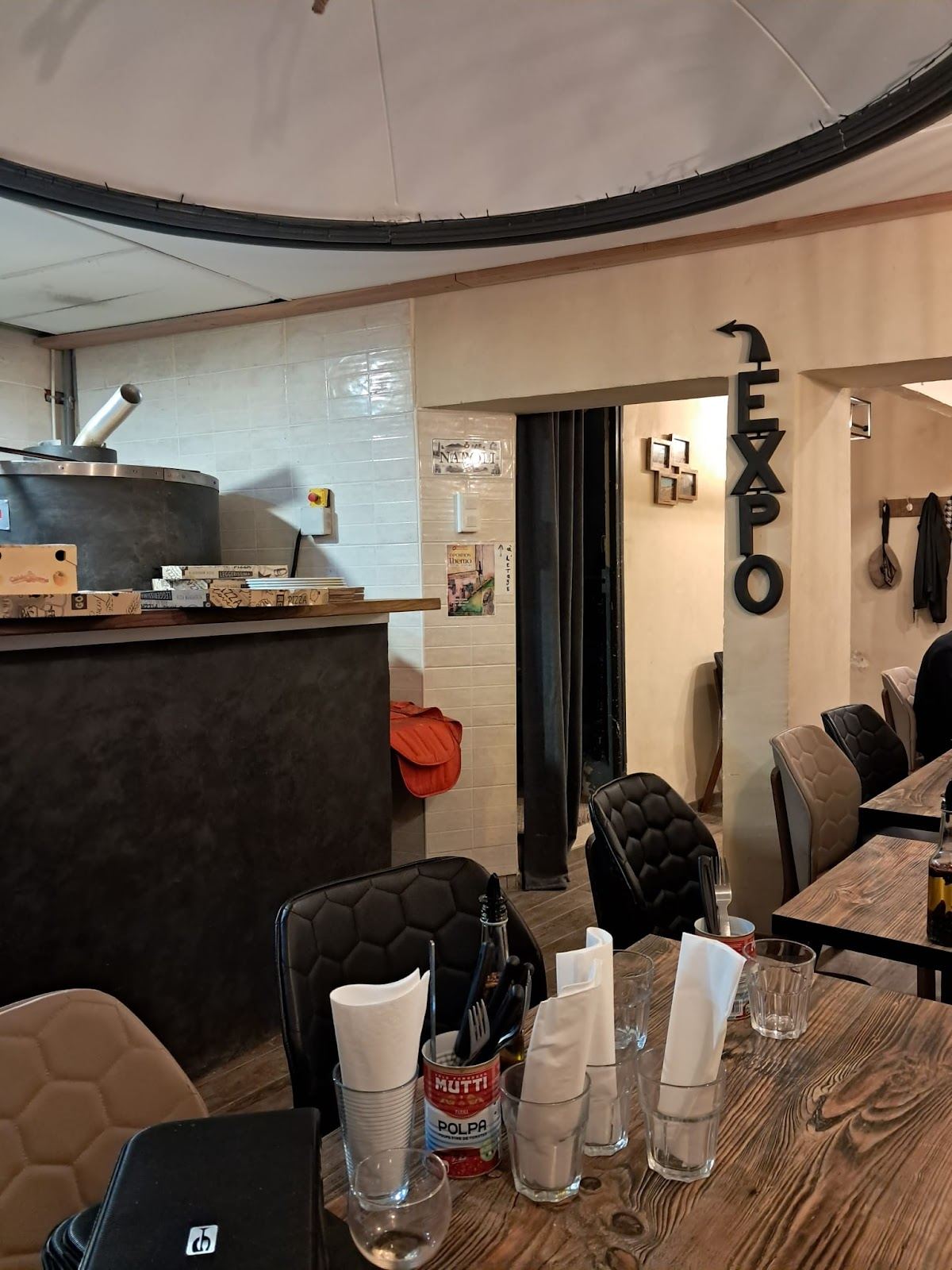 Intérieur de la pizzeria : tables en bois, four et passe